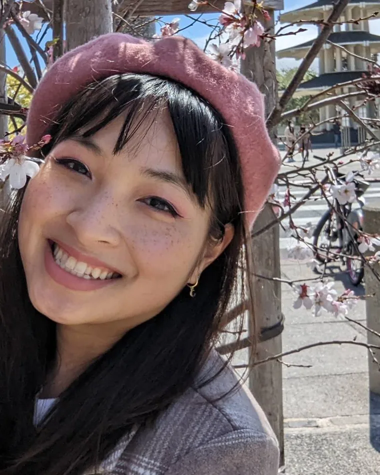 Denise Ngo in a pink beret, smiling under cherry blossoms in San Francisco's Japantown