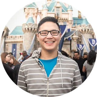 A smiling young man in glasses in front of Sleeping Beauty Castle