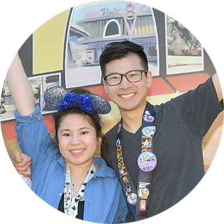 A couple in Mickey ears and pin lanyards cheering in the park