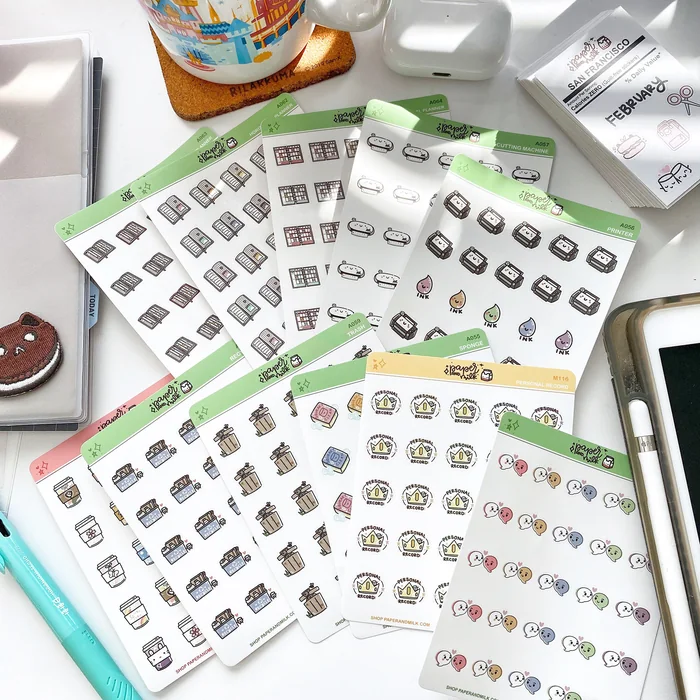 A fanned stack of Paper and Milk sticker sheets with small illustrated icons on a desk
