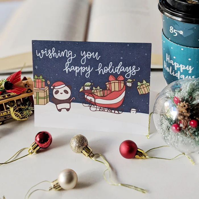 A navy holiday card reading 'wishing you happy holidays' with a panda and Santa's sleigh, surrounded by ornaments